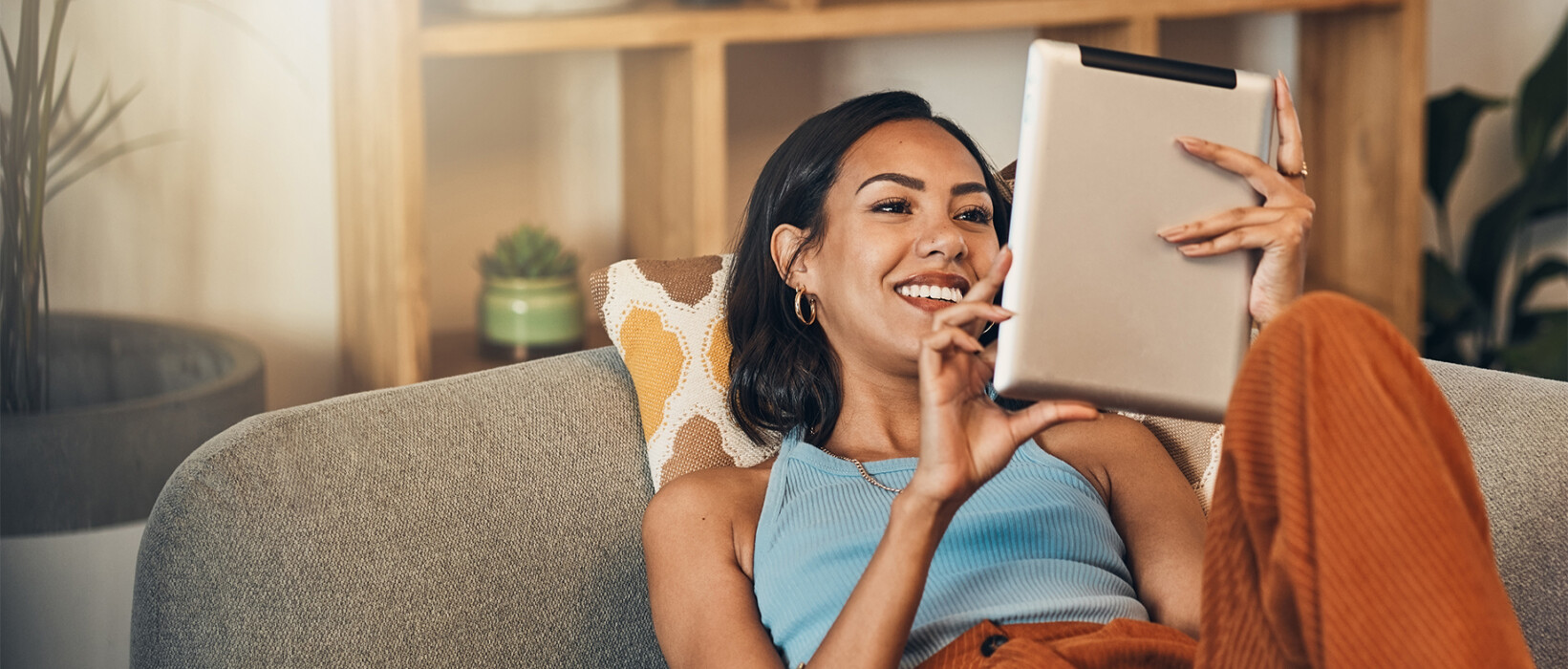 Woman relaxing on a couch while reading news on a tablet.