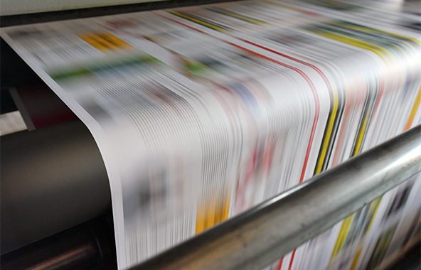 Newspapers moving quickly through a printing press.