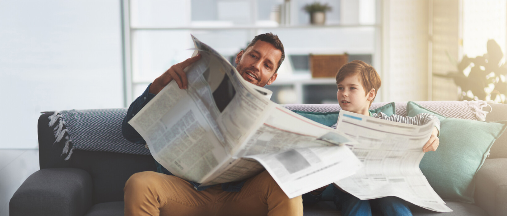 Adult and child reading newspapers together at home.
