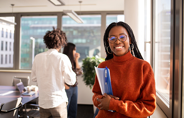 Student holding folders in a bright office setting.
